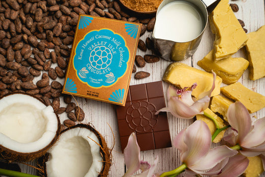 Valley Isle Chocolate bar with coconut pieces, flowers, and chocolate pieces on a wooden surface.