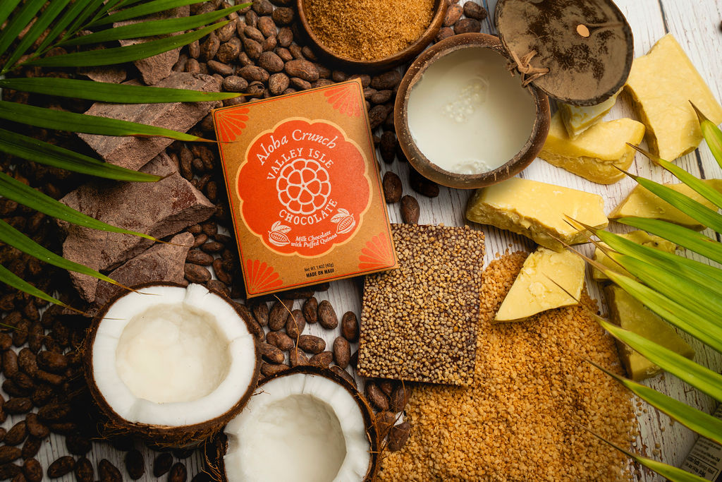 Box of Valleys Crunch Chocolates surrounded by coconuts, beans, and other natural elements on a wooden surface.