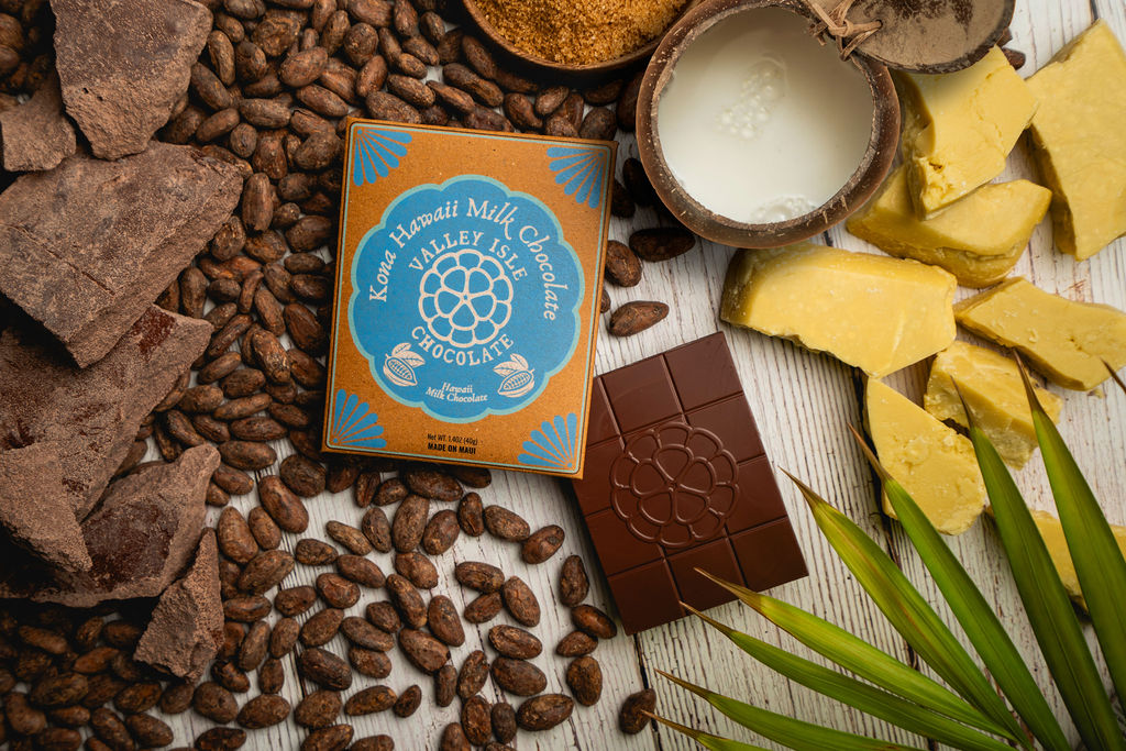 Kona Valley Chocolate packaging surrounded by cacao beans and chocolate pieces on a wooden surface.
