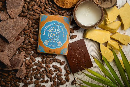 Kona Valley Chocolate packaging surrounded by cacao beans and chocolate pieces on a wooden surface.